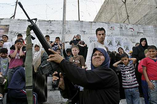 A Palestinian woman shoots in the air during a march by militants from the Al Aqsa Martyrs' Brigade