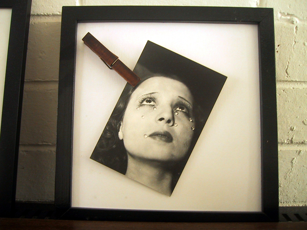 Glass-less picture frame containing a Man Ray postcard held in place by a clothes peg.