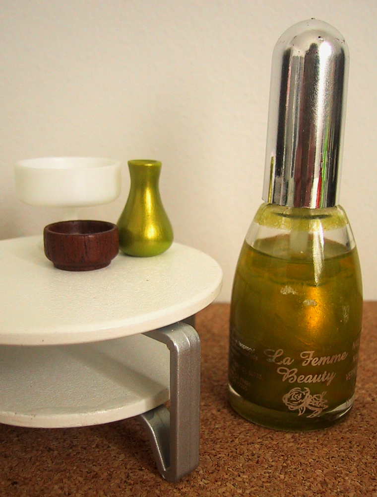 Modern dolls' house miniature coffee table, displaying two bowls and a green vase. On the floor next to it is a full-sized bottle of nail varnish.