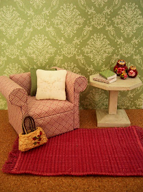 Modern dolls' house miniature scene with green and cream patterned walls, a pink and white armchair and white side table on a pink woven floor rug.