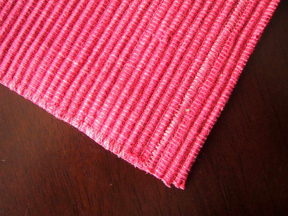 Piece of pink woven placement, cut along a line of zig zag stitching, and three rows up at the top.