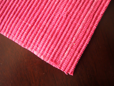 Piece of pink woven placement, cut along a line of zig zag stitching, and three rows up at the top.