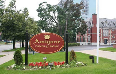 Wooden sign in front of a large, attractive residential building. The sign reads Amigone Funeral Home.