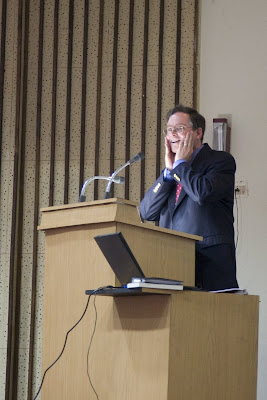 Jim Fruchterman, giving a speech as a podium, grabbing his cheeks in surprise