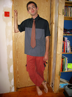 A chap (me) in a black shirt, red trousers which stop above the ankle, and a red tie standing in a doorway.